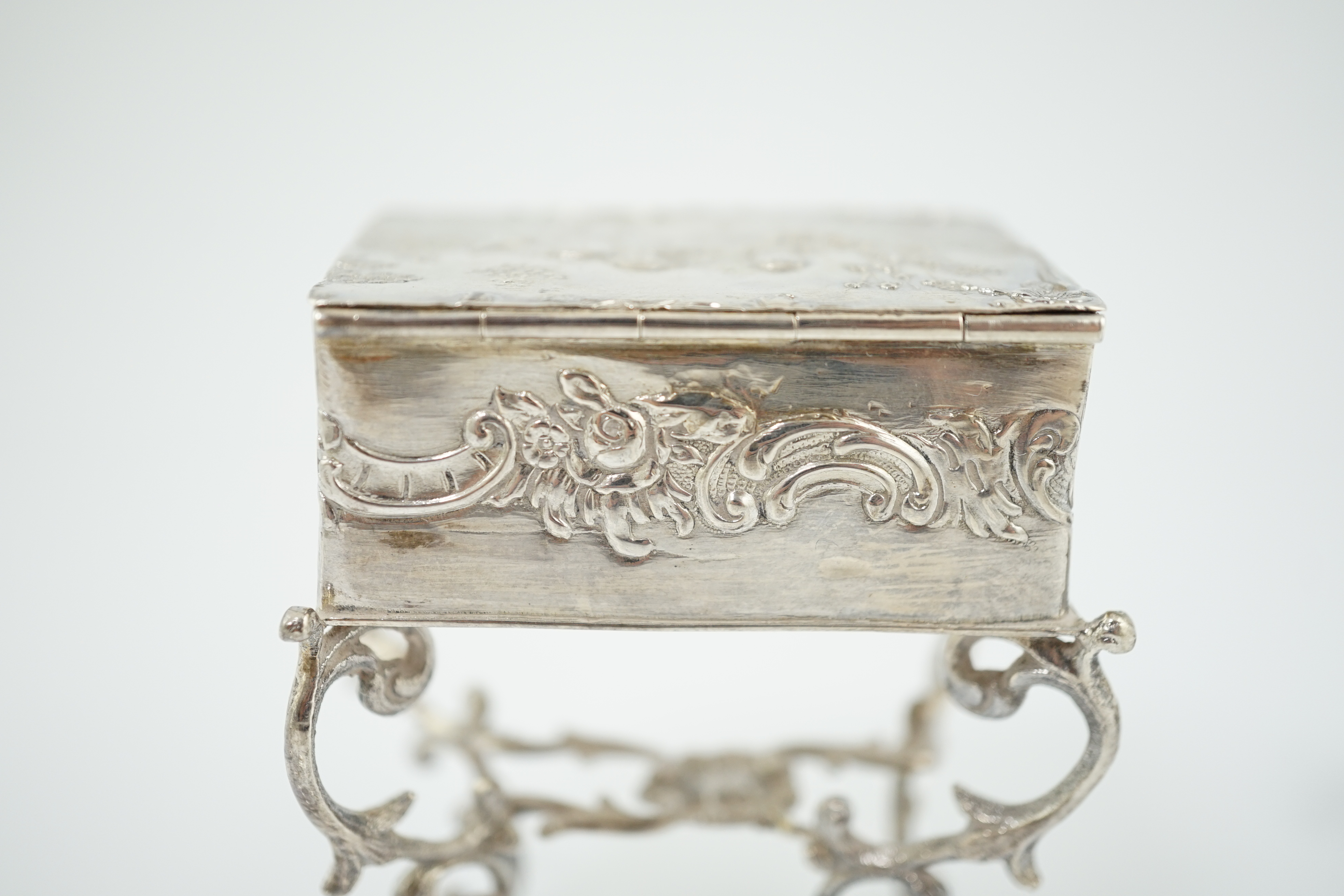 A late 19th century continental embossed silver miniature model of grand piano, length 53mm, together with a similar model of a table/desk on ornate scroll supports